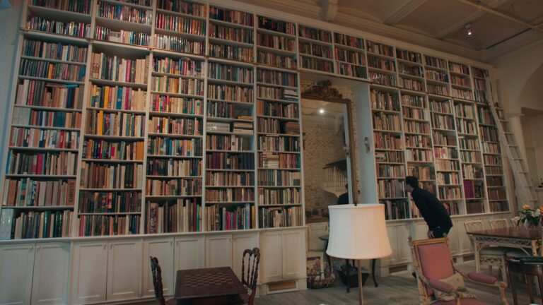 Floor-to-ceiling bookshelves filled with books, ladder, and a person looking at books.