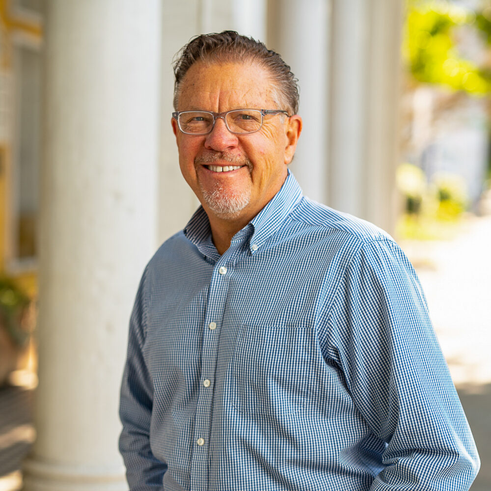 Jody Kielbasa portrait. Man with glasses smiles in front of white columns.