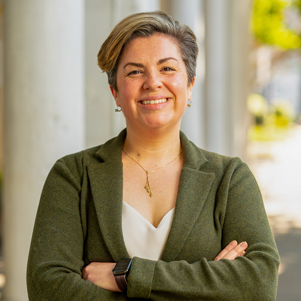 Erica Barnes smiles in a green blazer, arms crossed, in front of columns.