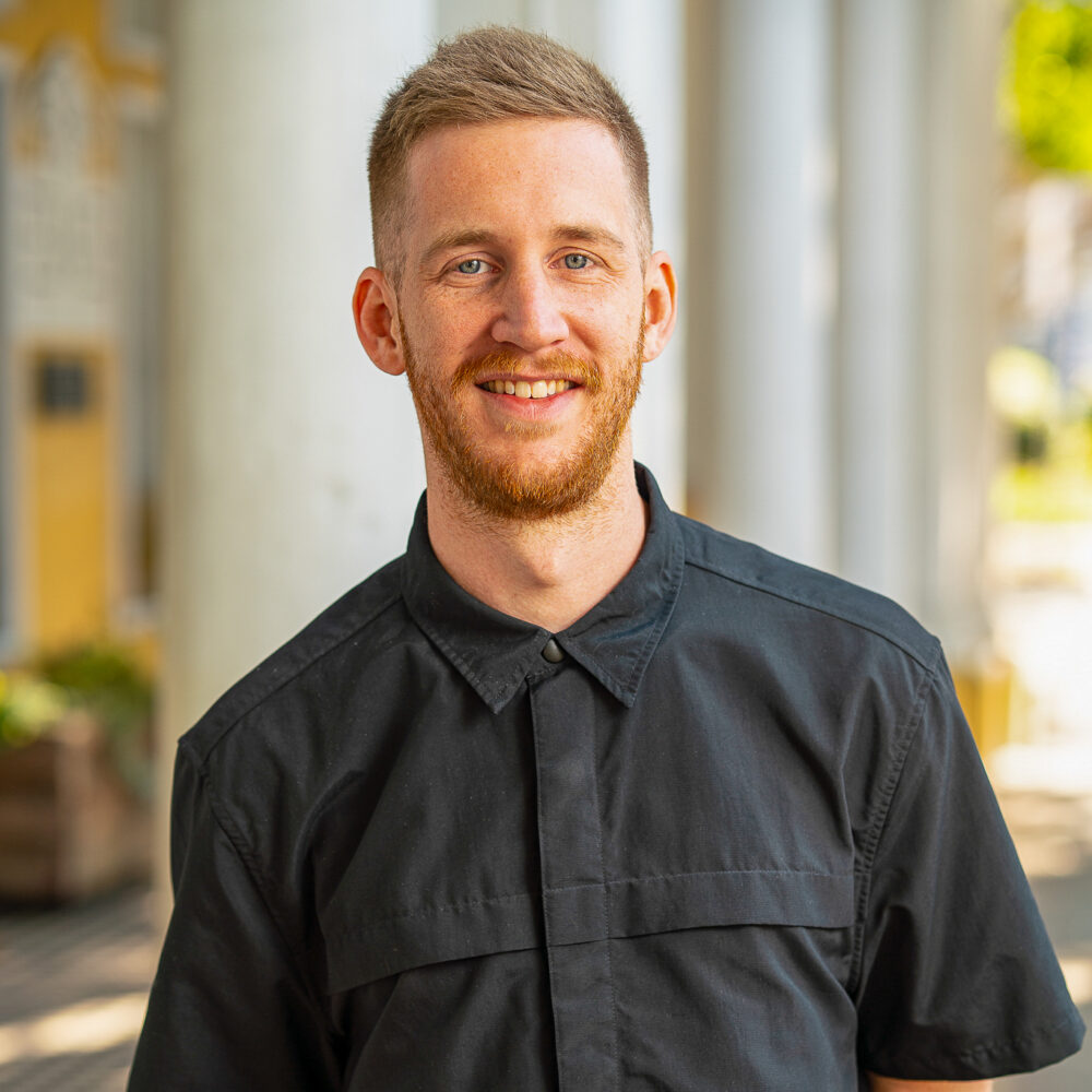 Robert Dunnenberger smiles in a black shirt with white pillars in the background.