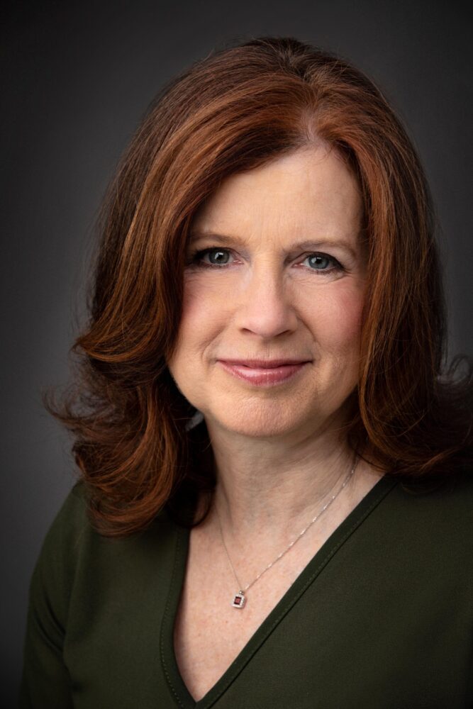 Headshot of Janet Graham Borba, smiling with red hair and wearing a green top.