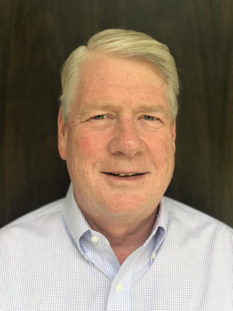 Headshot of John F. Harris, smiling and wearing a light blue shirt.