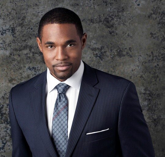Actor Jason George in a stylish navy suit and tie, looking confident.