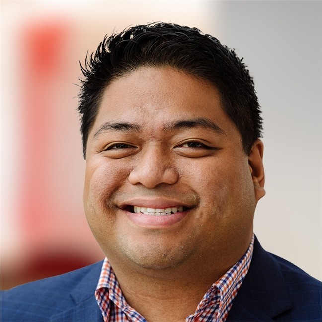 Marc Paulo Guzman smiles in a blue jacket and checkered shirt.