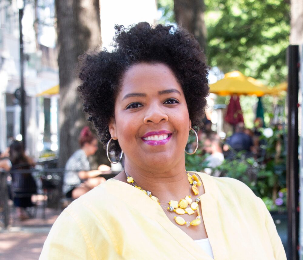 Andrea Copeland, smiling woman with natural hair, wearing a yellow shirt and necklace.