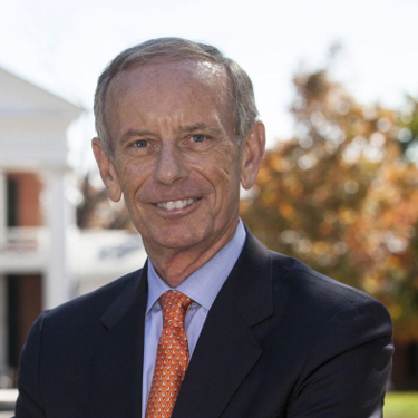 Pat Hogan, wearing a suit and orange tie, smiling outdoors.