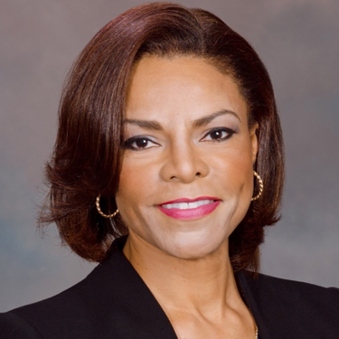 Professional headshot of Rita McClenny, smiling with short brown hair and gold hoop earrings.