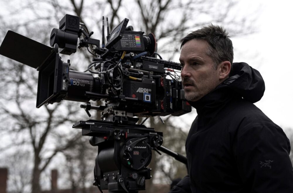 Director Scott Cooper behind a Panavision camera on set, wearing a black jacket.