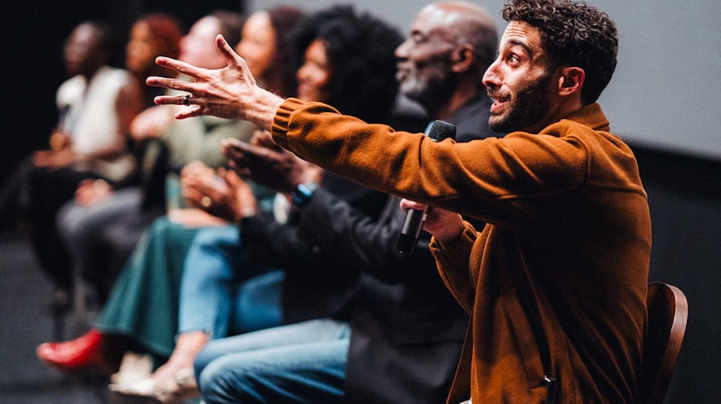 Speaker addressing a film panel, gesturing with hand and holding microphone.