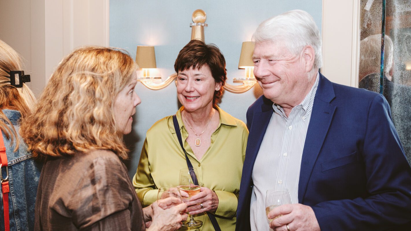 Three people chatting and holding drinks at an event.