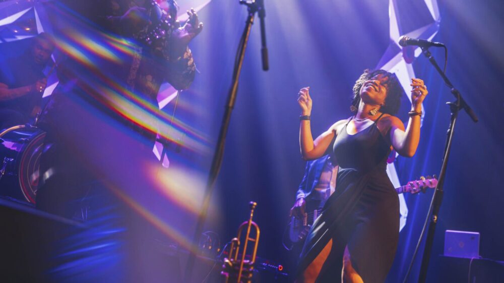 Singer performing on stage with band, bathed in blue light. NEA 2024 performance.