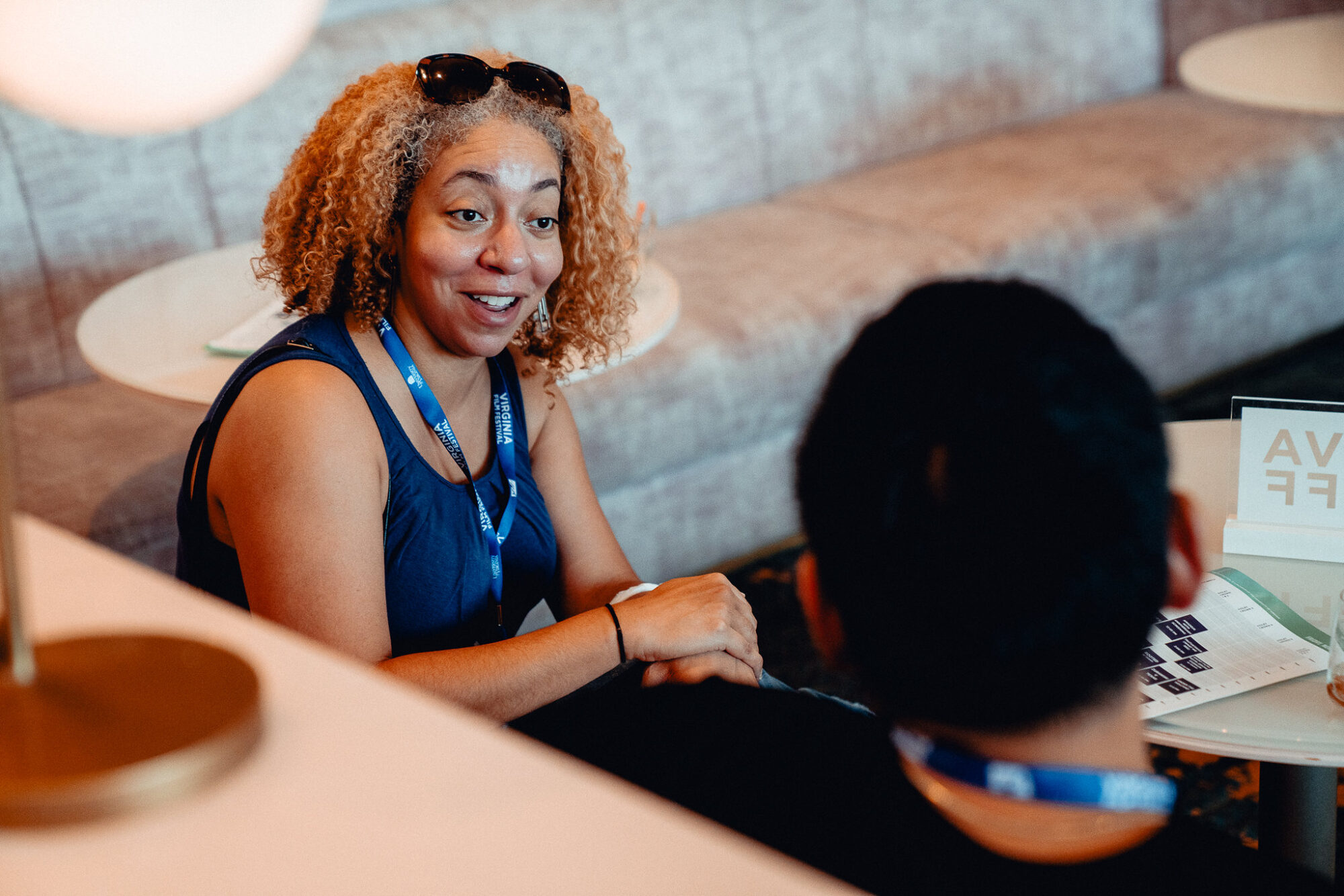 Woman with curly hair wearing a conference badge, in conversation. Connection Point.