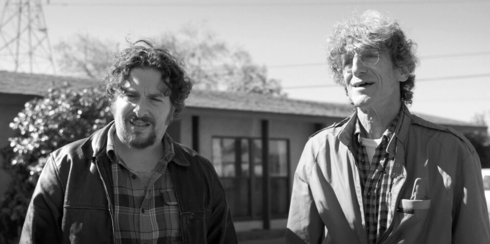Black and white photo of two men, possibly from the film "Burt," outside a house.