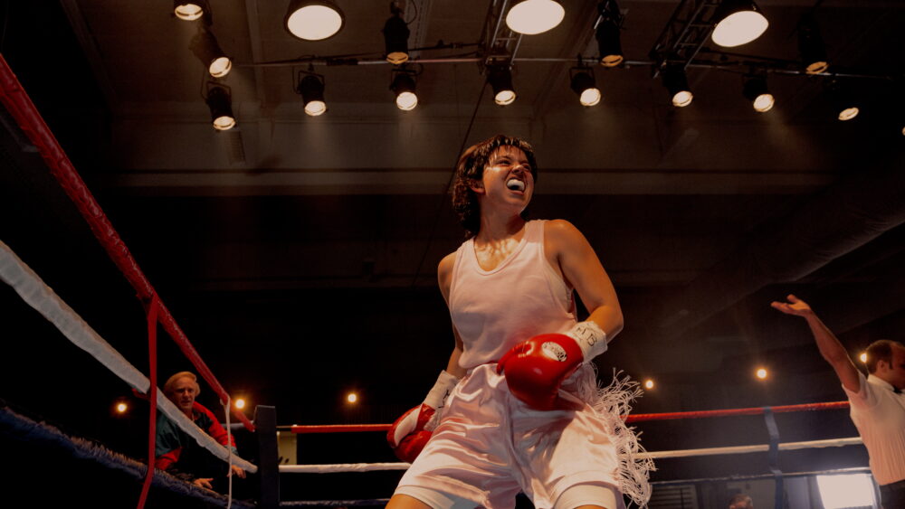 Scene from CHRISTY. Female boxer celebrating a win in the boxing ring, wearing red gloves.
