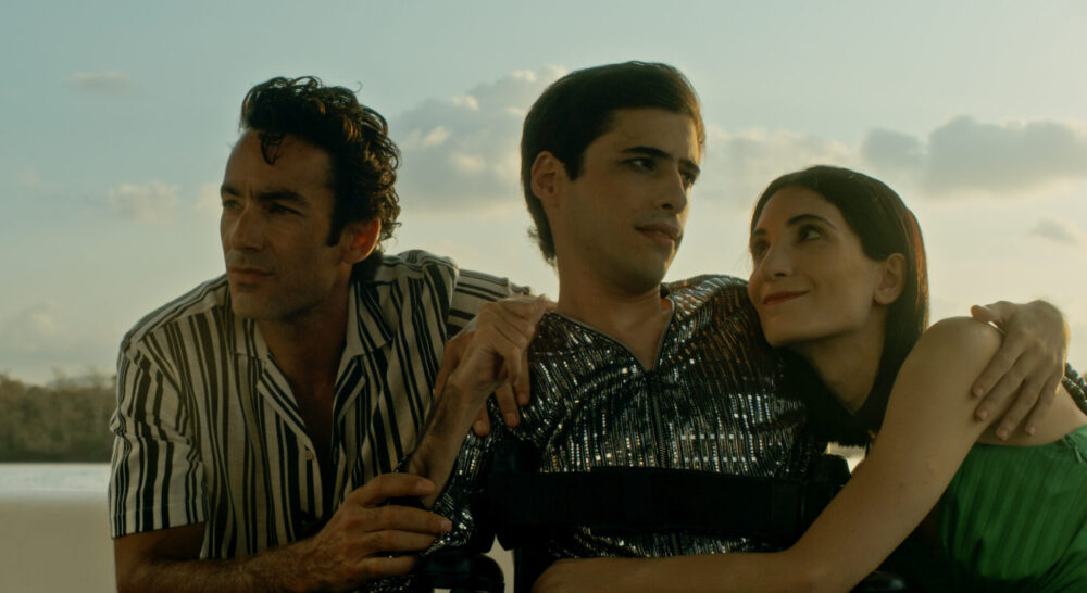 Three friends embrace by the water in "Espina": man in wheelchair, woman, man.