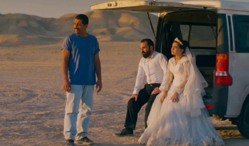 Bride in wedding dress with men by van in desert
