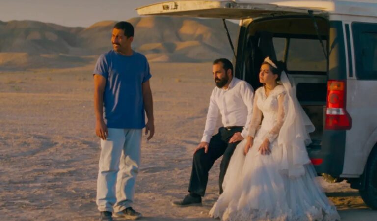 Bride in wedding dress with men by van in desert