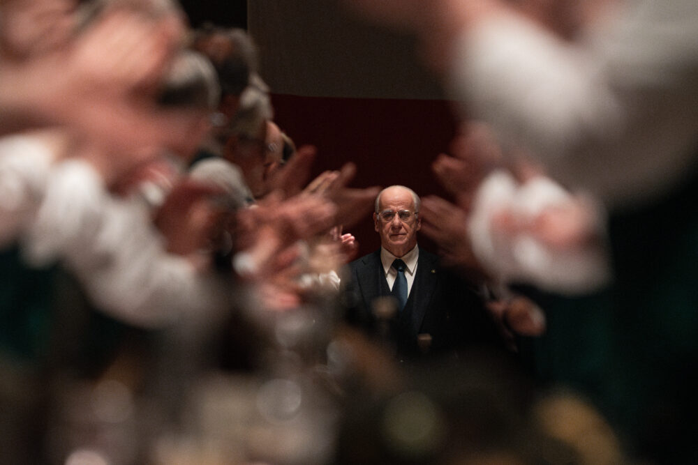 Man in suit amidst applause, possibly at La Grazia event. Bald man with tie in focus.