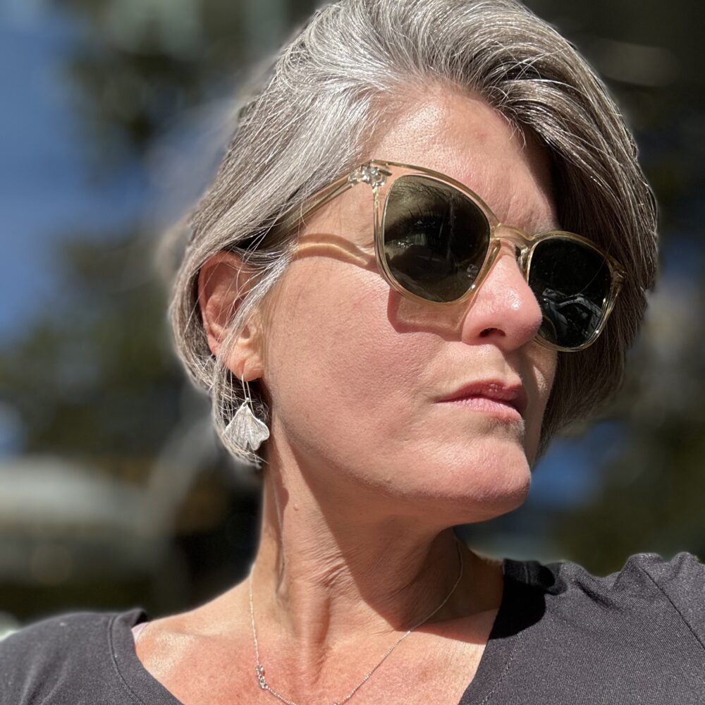 Woman with gray hair wearing sunglasses and a silver necklace.