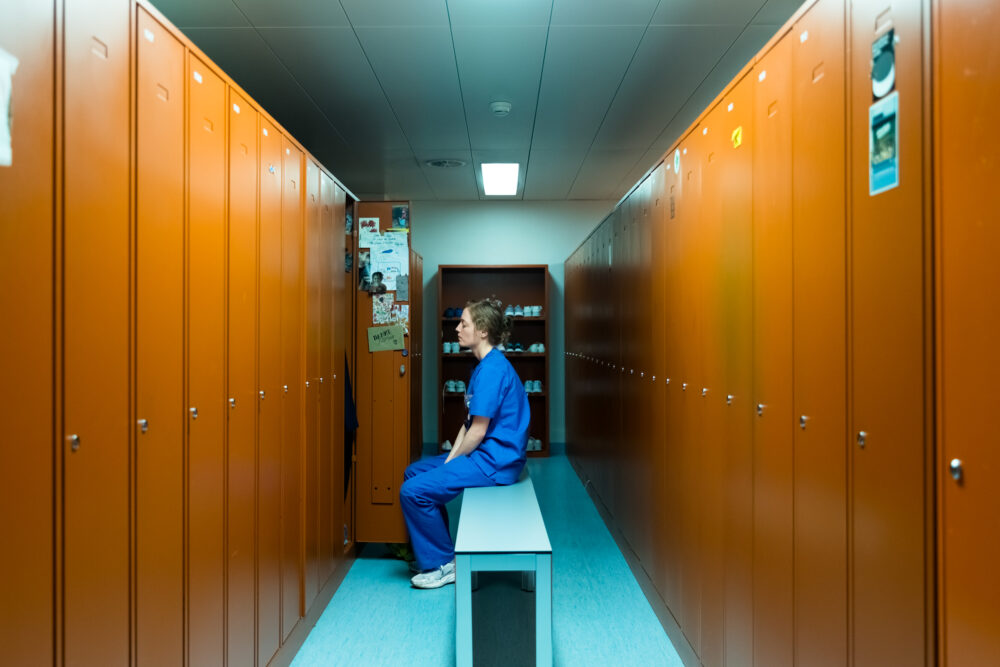 Healthcare worker in blue scrubs sits in locker room.