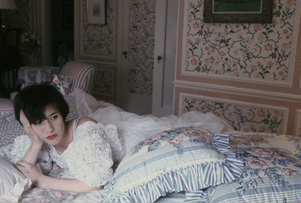 Still from "Metropolitan" (35th Anniversary): Audrey Rouget in an ornate floral room, lying on a floral bed.