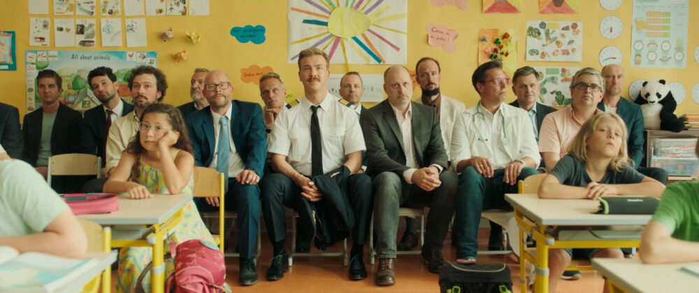 Classroom scene with adults and children sitting at desks.