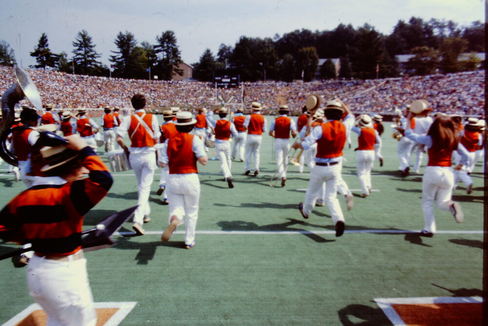 Marching band performs on a football field before a crowd.