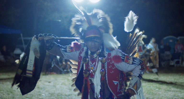 Scene from POWWOW PEOPLE. Powwow dancer in traditional regalia performing at night.