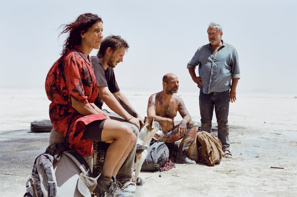 Group of people and a dog resting in a desolate landscape, possibly related to the movie "SirÂt".