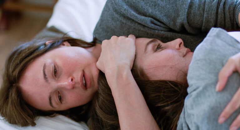 Two women lying together in bed, embracing affectionately.