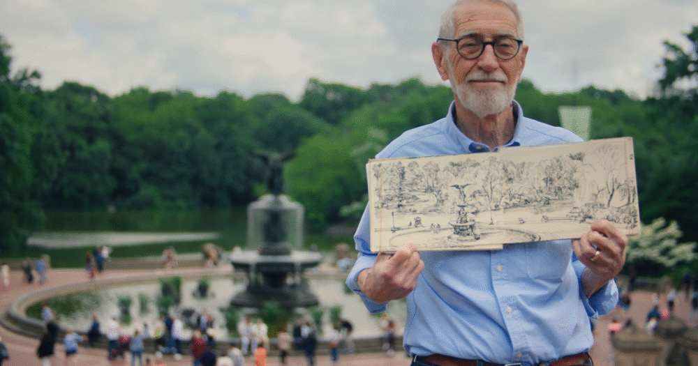 Film still from SITTING STILL. Man with glasses in a crowded park holding an illustration.