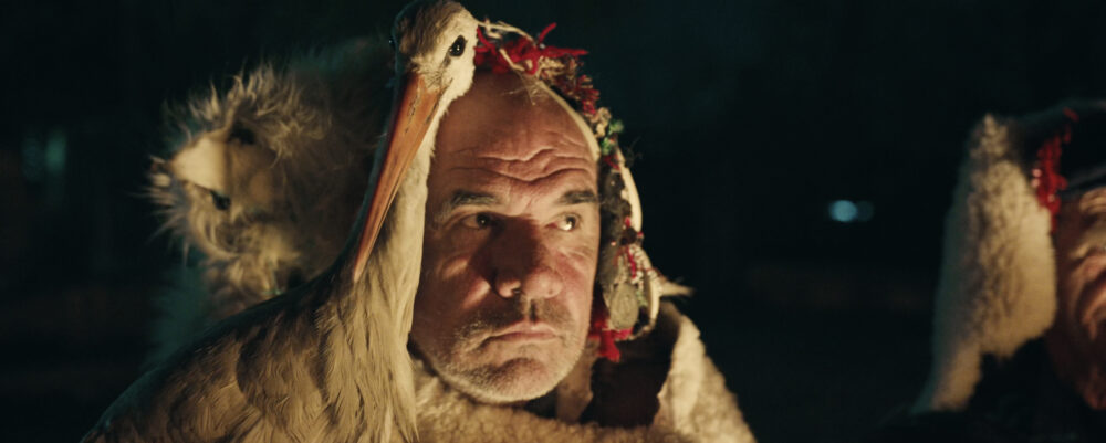 Man with stork on shoulder, wearing traditional attire. The Tale of Silyan.