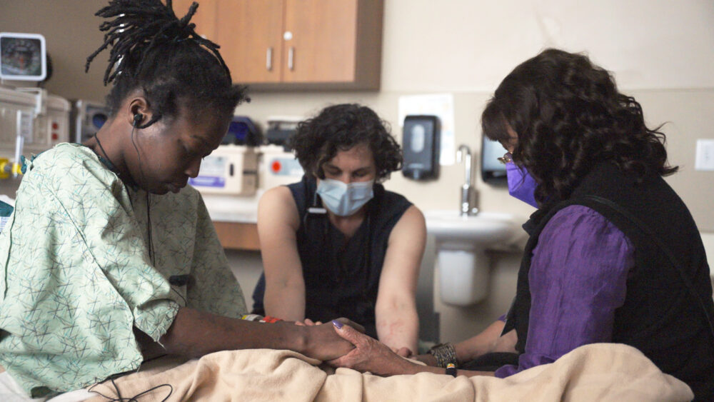 Patient receiving bedside support from chaplain and doctor.