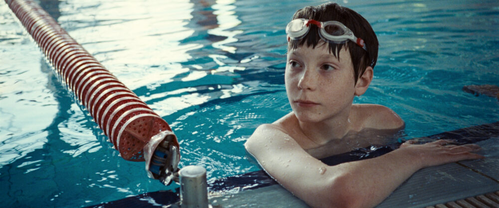 Boy wearing goggles in a swimming pool with a red lane rope