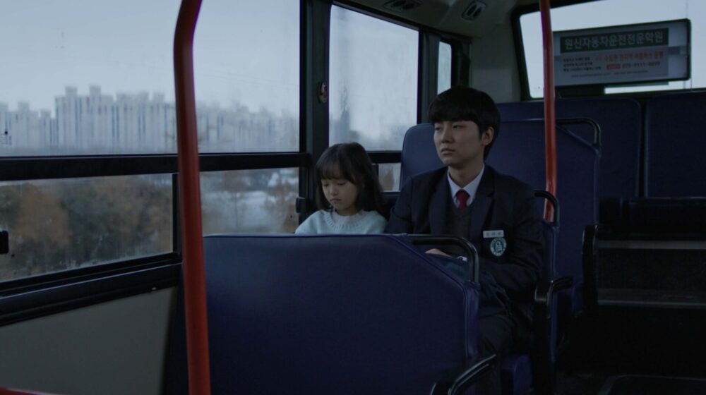 Teen boy and young girl on a bus. Winter light filters through the window.