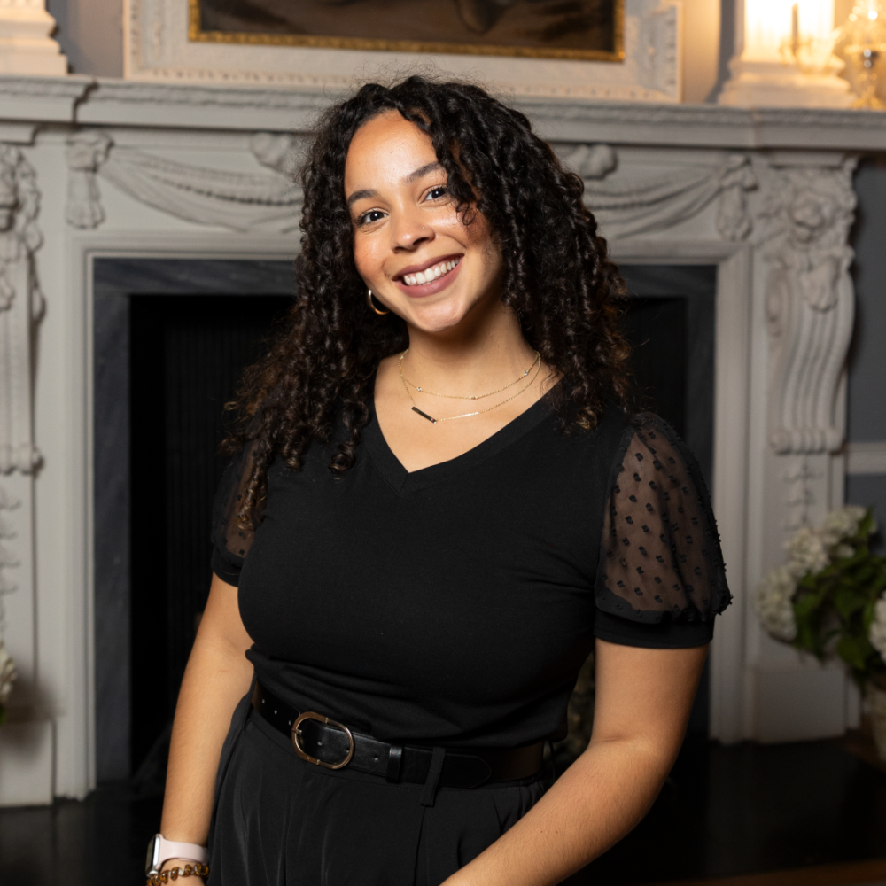 Nathaly Abreu smiling in a black outfit in front of a fireplace