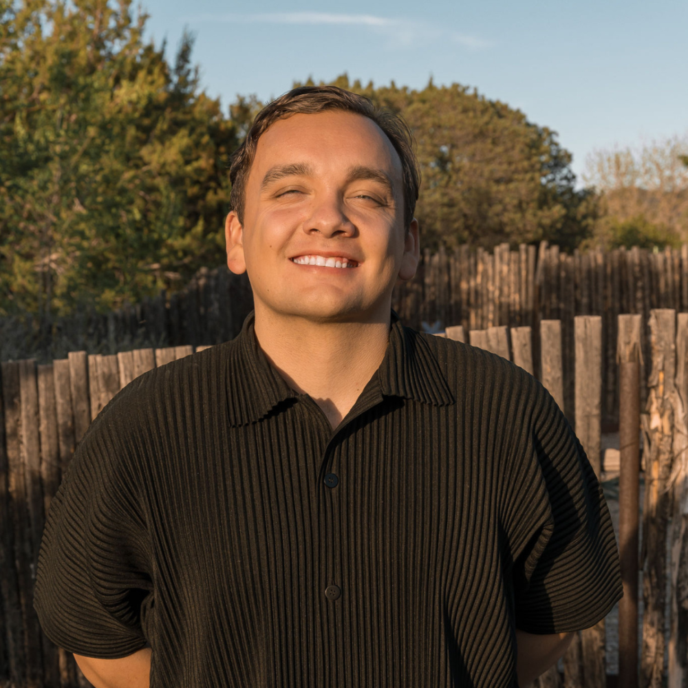 Cole Forrest smiles outdoors in front of a wooden fence.